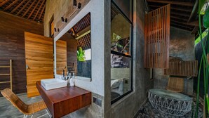 Ein modernes Badezimmer mit einem Holzkosmetikschrank, einem großen Spiegel und einer Sitzecke mit einem Rattanstuhl.