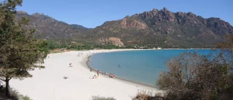 A beach with clear blue water, sandy shore, and mountains in the background.