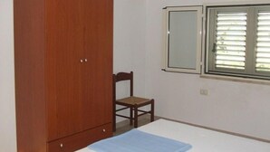 Une chambre avec une armoire en bois, un lit simple, une chaise et une fenêtre avec des stores.