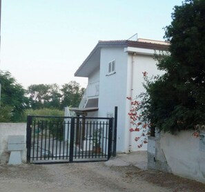 Un bâtiment à deux étages, à la façade blanche, doté d’un balcon à l’étage supérieur et d’un portail en métal noir à l’entrée.