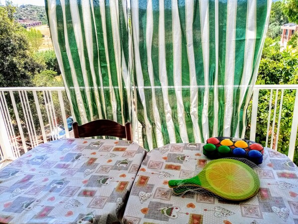 A balcony with a table covered in a patterned tablecloth, a chair, and colorful balls and a tennis racket.