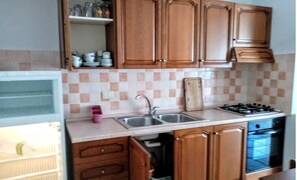 A kitchen with wooden cabinets, a sink, a stove, and a tiled backsplash. - a Stone's Throw Away From Foximannana in the Foreground - Tertenia (Tertenia)