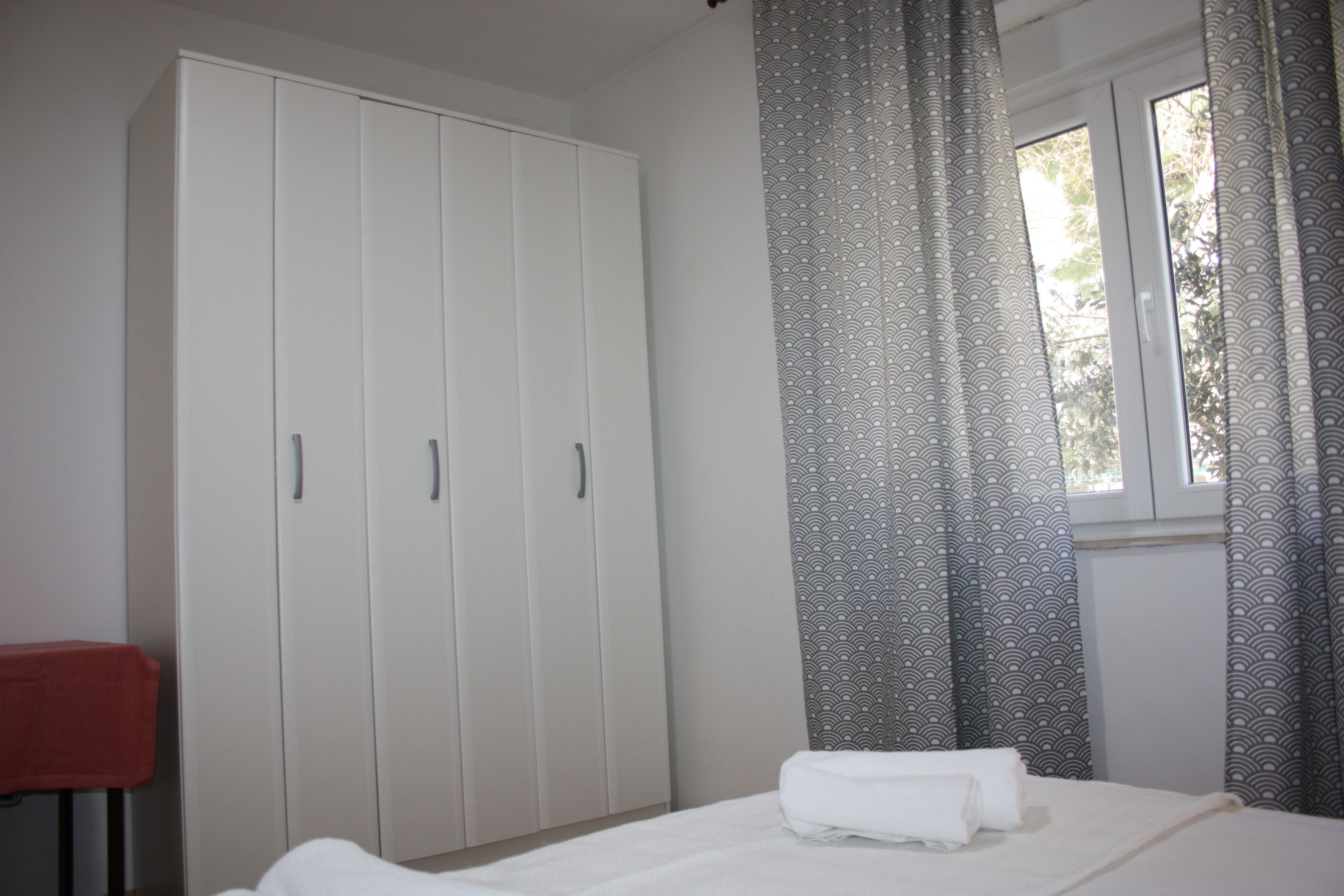 A bedroom with a bed, a wardrobe, and a window with curtains.