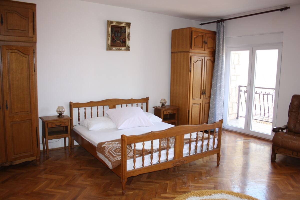 A bedroom with a wooden bed, a nightstand, a wardrobe, and a view of the outside balcony.