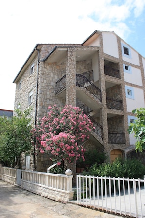 A multi-story building with stone facade, balconies, and a white fence.
