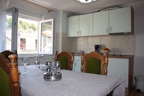 A dining area with a table set for four, a window with a view of buildings, and a kitchen with light green cabinets.