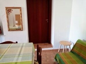 Une pièce avec une table à carreaux, un miroir, une porte en bois, un canapé à rayures vertes et un petit tabouret.