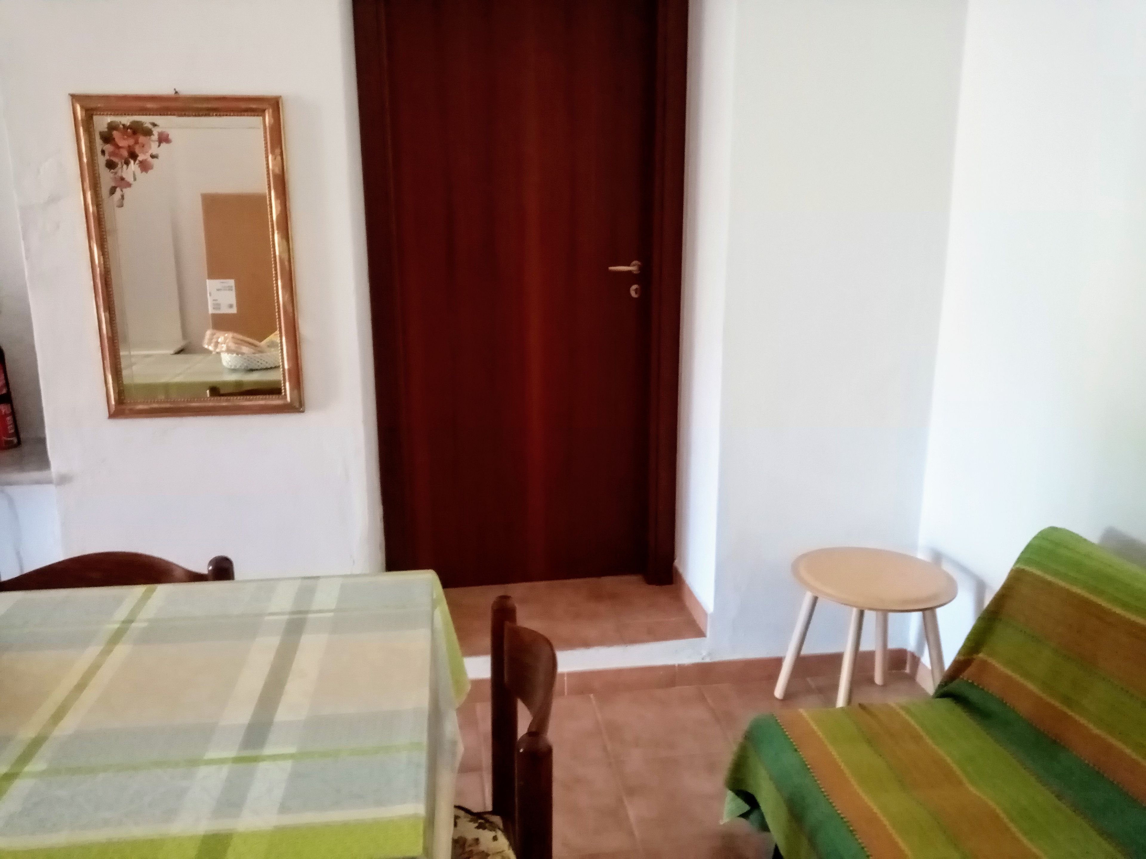 Una habitación con una mesa a cuadros, un espejo, una puerta de madera, un sofá con rayas verdes y un taburete pequeño.