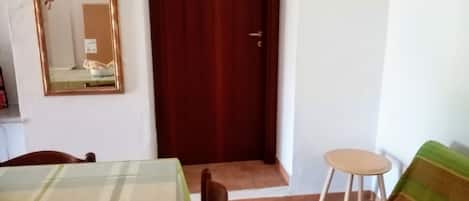 Una habitación con una mesa a cuadros, un espejo, una puerta de madera, un sofá con rayas verdes y un taburete pequeño.