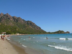 A beach with clear waters, rocky mountains in the background, and people swimming. - Tertenia Ground Floor South 3 min Walk From the sea (Tertenia)