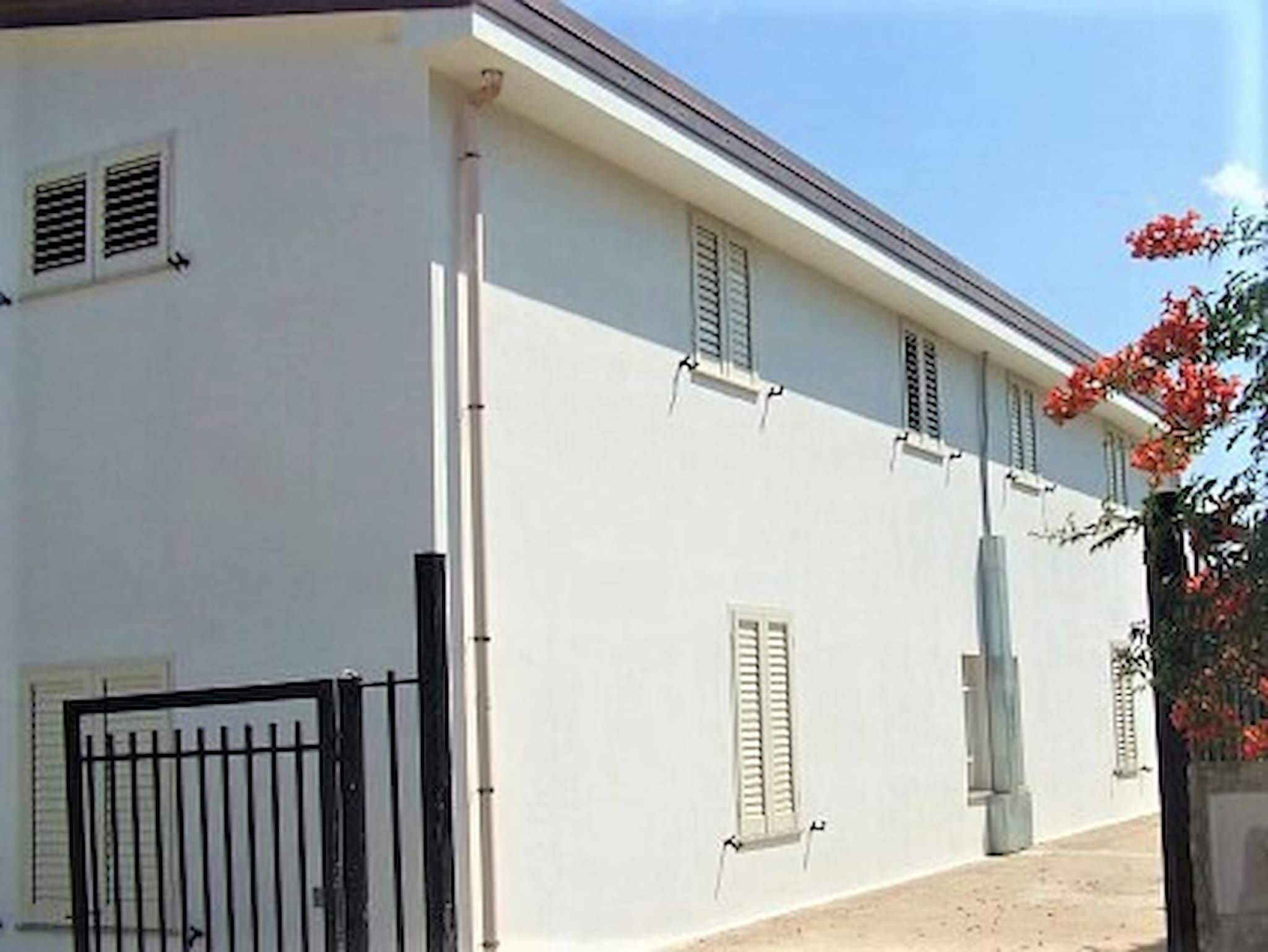 A white building with shutters, a gated entrance, and a clear sky.