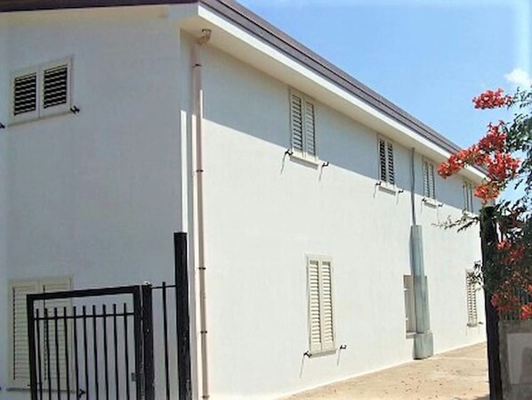 Un edificio blanco con persianas, un acceso con portones y cielo despejado.