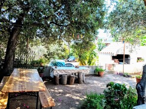 An outdoor patio with a wooden table and benches, surrounded by trees and potted plants. - Tertenia Ground Floor South 3 min Walk From the sea (Tertenia)