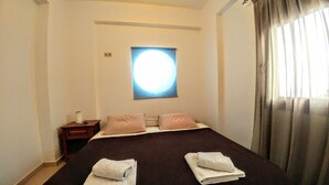 A bedroom with a large bed, a nightstand, a wall-mounted light, and a window with curtains. - Sunny Cozy Home AMAZING SEA VIEW (Archanes-Asterousia)