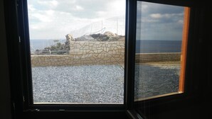 A view through a window with a stone wall and pebbles in the foreground, leading to a rocky landscape and the sea in the background. - Sunny Cozy Home AMAZING SEA VIEW (Archanes-Asterousia)