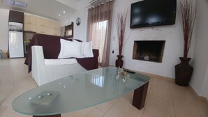 A living room with a glass-top coffee table, a sofa, a television mounted on the wall, and a fireplace. - Sunny Cozy Home AMAZING SEA VIEW (Archanes-Asterousia)