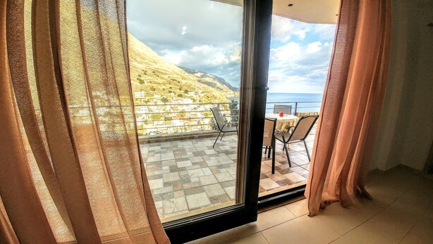 A balcony with a table and chairs, overlooking a coastal town and the sea. - Sunny Cozy Home AMAZING SEA VIEW (Archanes-Asterousia)