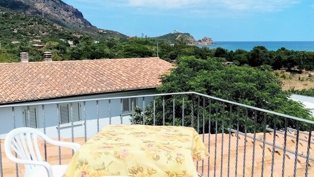A balcony with a yellow floral tablecloth, a white chair, and a view of a coastal landscape with mountains and the sea. - Always on Foot 3 min to the Beach Center With Double Terrace (Tertenia)