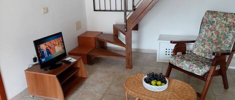 A living room with a television, wooden furniture, a staircase, and a floral chair.