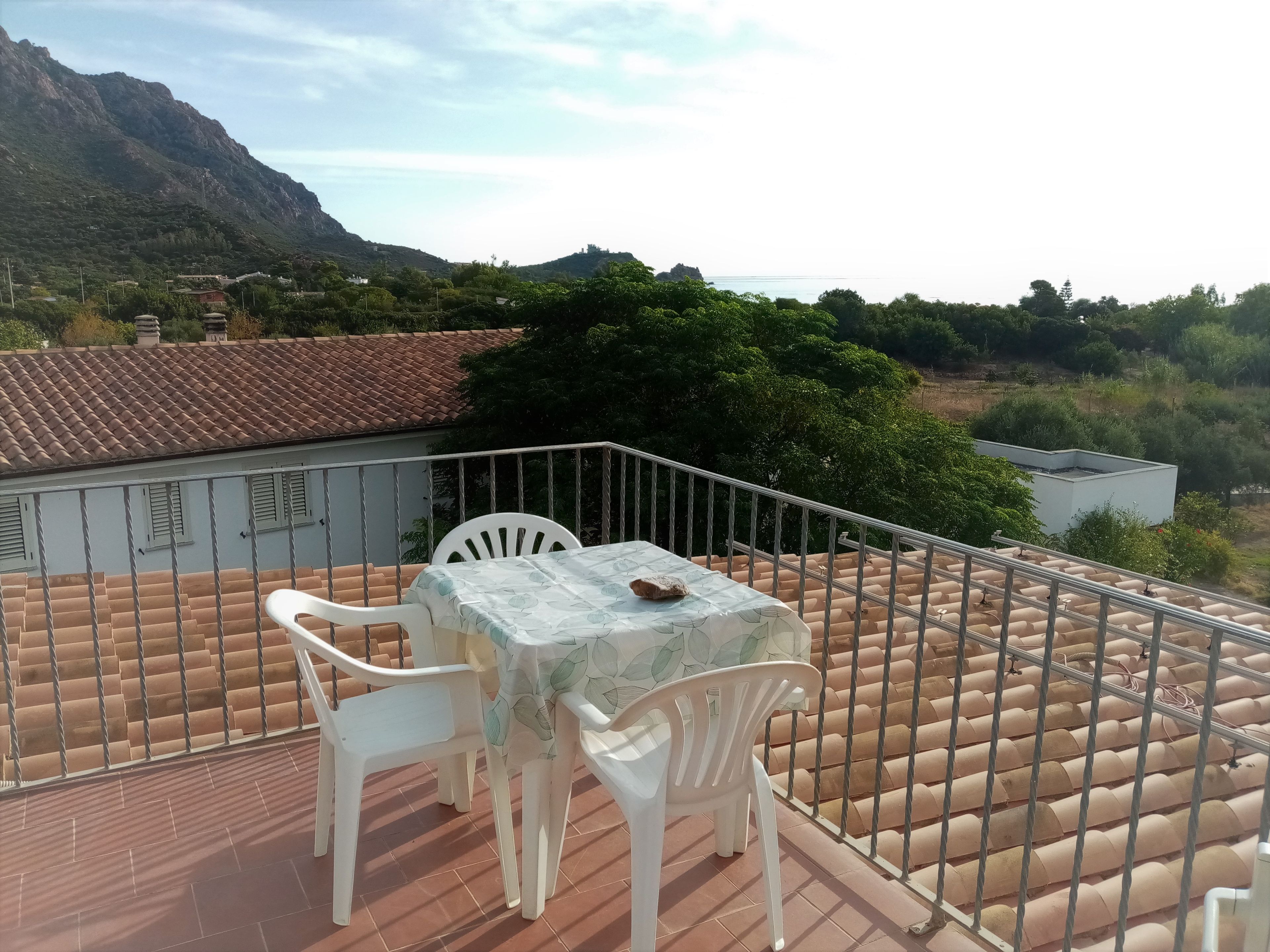 Eine Terrasse mit Tisch und Stühlen, Blick auf die umliegende Landschaft und ein Gebäude mit Ziegeldach.