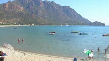 A beach with clear water, boats, and mountains in the background.