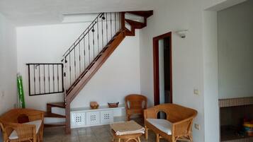 A living room with a wooden staircase, wicker furniture, and a fireplace.