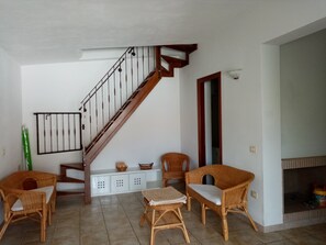 A living room with a wooden staircase, wicker furniture, and a fireplace.