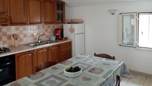 A kitchen with wooden cabinets, a sink, a stove, and a refrigerator. There is a table with a tablecloth and a basket of fruit. - Always on Foot 3 min to the Beach Center With Double Terrace (Tertenia)