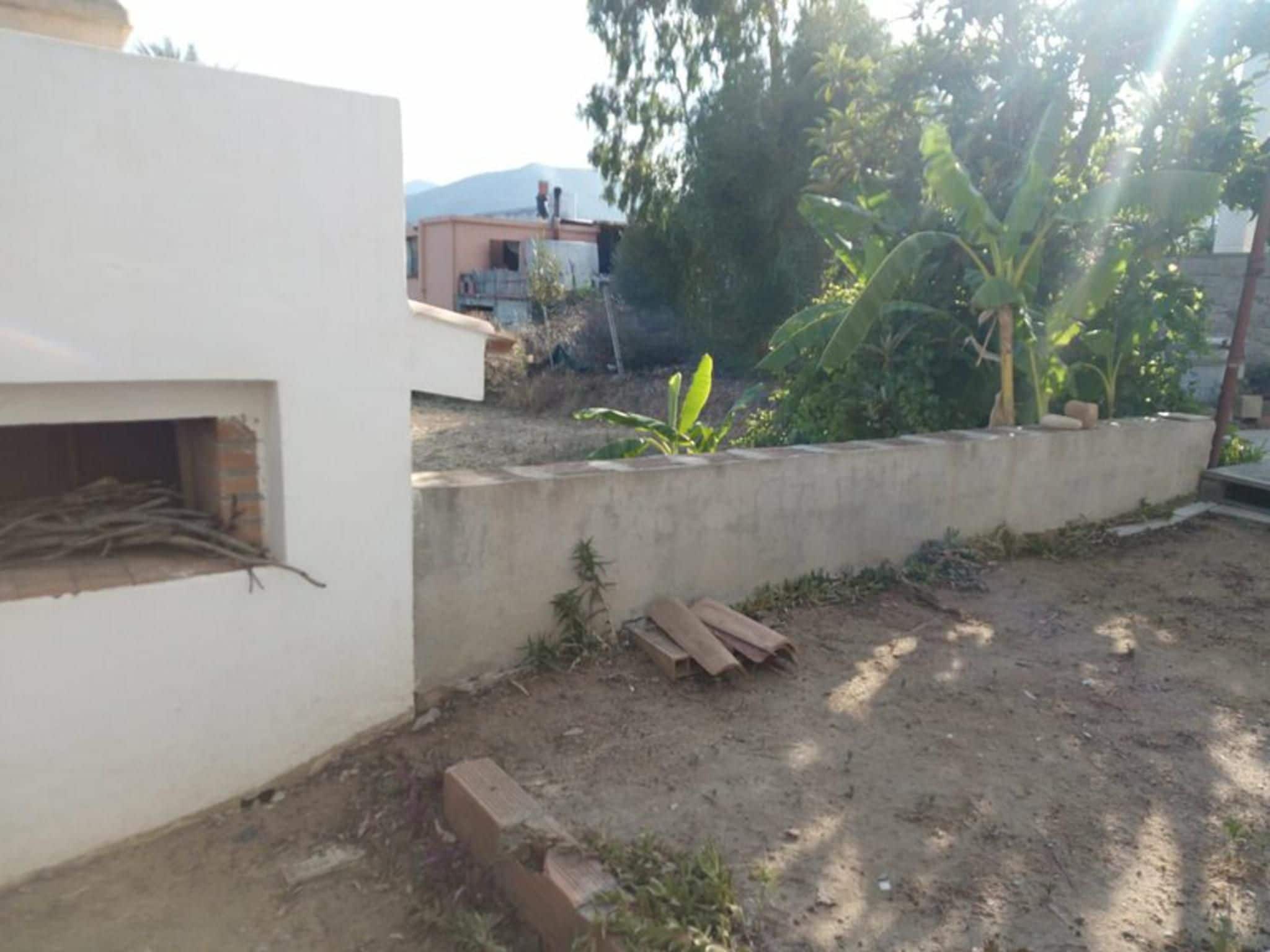 A courtyard with a concrete wall, a small garden with plants, and a pile of wooden planks.