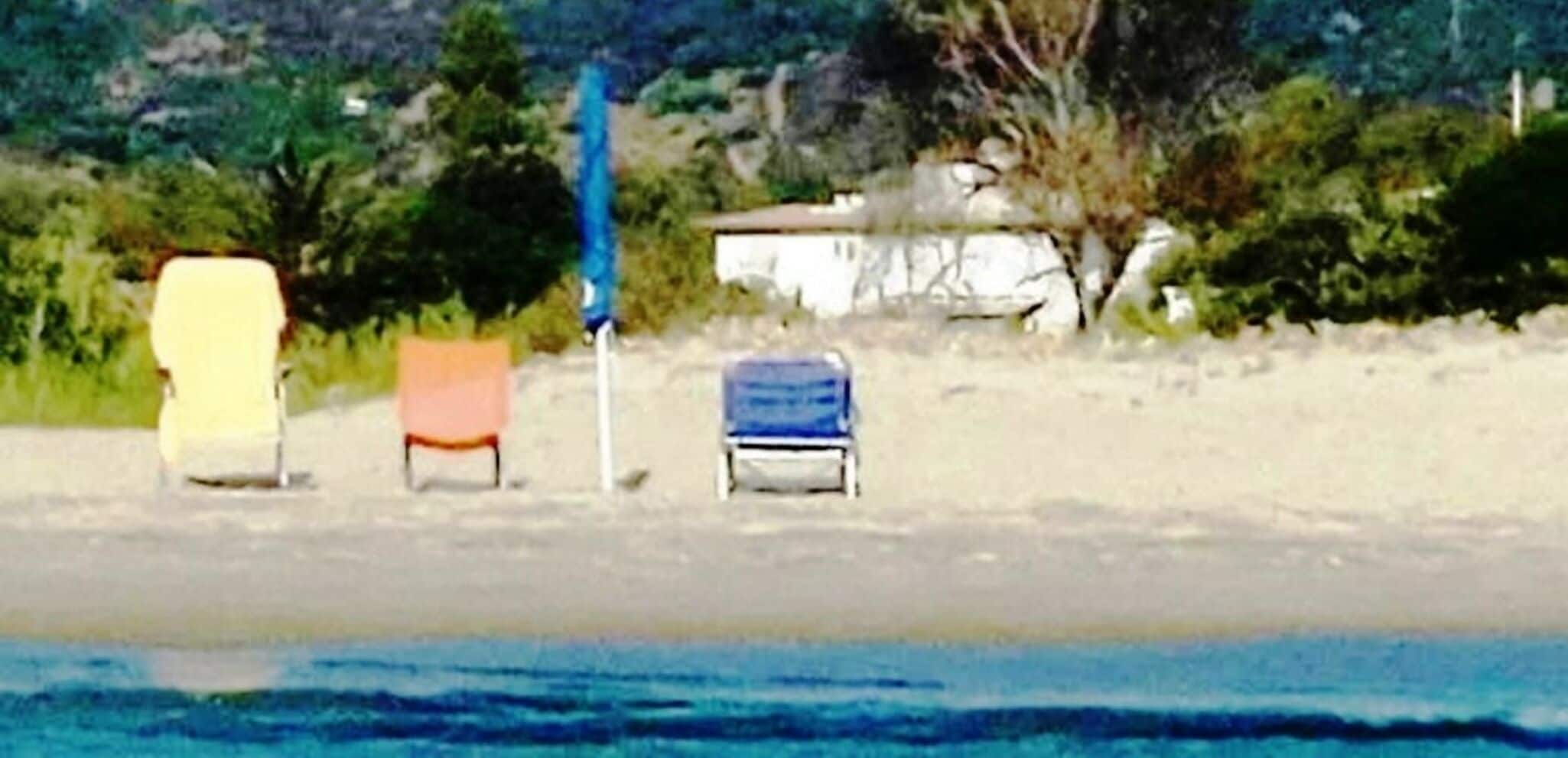 Escena de playa con tres sillas y una sombrilla azul.