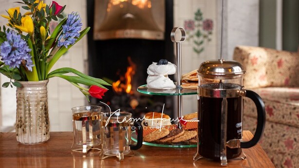 Een tafel met een koffiepot, glazen, een vaas met bloemen en gebak.