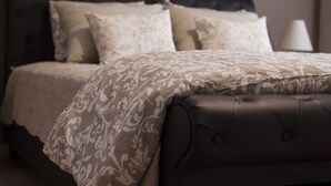 A neatly made bed with a patterned bedspread and several pillows, a dark headboard, and a bedside lamp.
