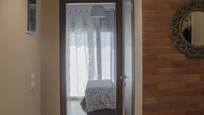 A hallway with a wooden floor leading to a bedroom with a bed and a window with curtains.
