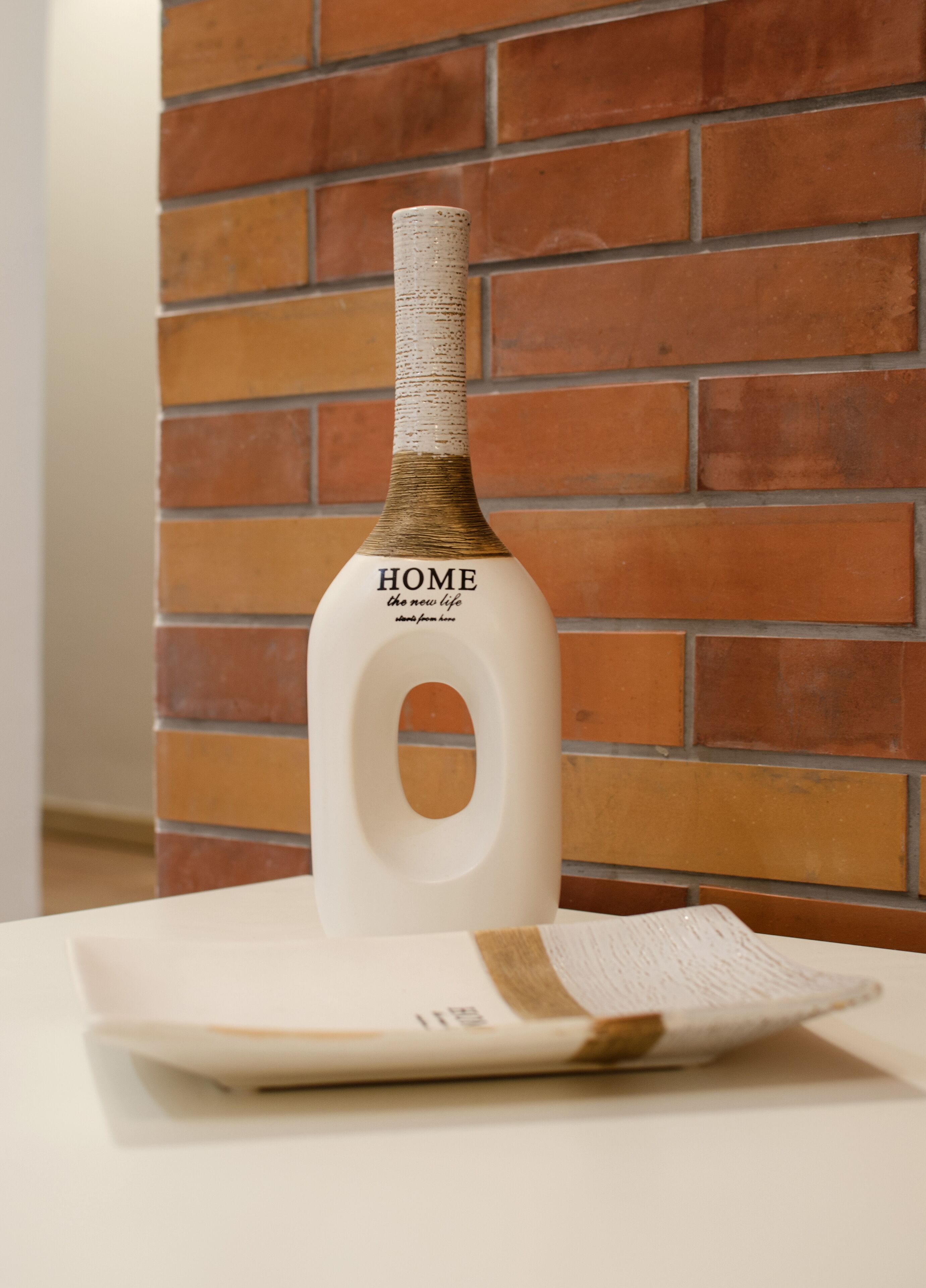 A bottle with the label "HOME the new life" on a white surface against a brick wall.