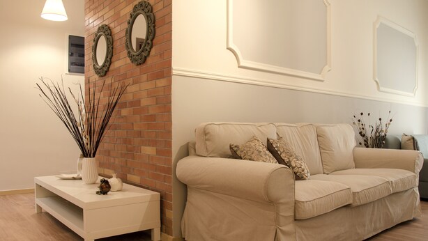 A living room with a beige sofa, a white side table, and decorative wall mirrors.