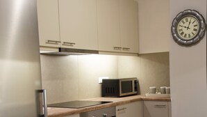 A compact kitchen with a stainless steel refrigerator, a microwave, and a built-in oven. There are wooden cabinets and a light-colored countertop.
