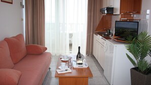 A compact living space with a sofa, a dining table with a bottle and glasses, a TV, and a kitchen area. - Apartments Ivan (Omis)