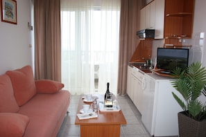 A compact living space with a sofa, a dining table with a bottle and glasses, a TV, and a kitchen area.