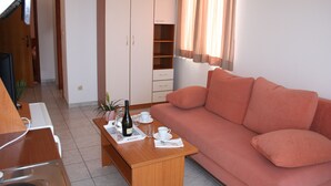 A living room with a sofa, a wooden coffee table with a bottle and glasses, a TV, and a wardrobe. - Apartments Ivan (Omis)