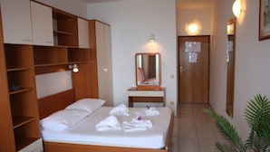 A hotel room with a wooden bed, a bedside table with a mirror, a wardrobe, and a potted plant. - Apartments Ivan (Omis)