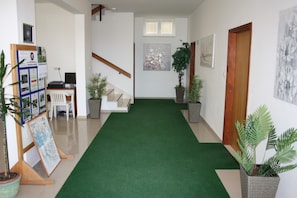 Un couloir avec un tapis vert, des plantes en pot, un escalier et une porte en bois.