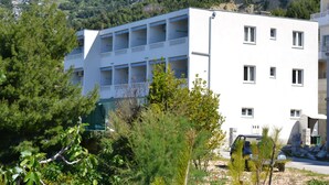 A multi-story building with balconies, surrounded by greenery and mountains in the background. - Apartments Ivan (Omis)