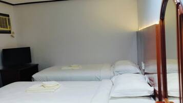Habitación de hotel con dos camas, un tocador de madera, un espejo, un cartel de 'No Fumar' y una botella de agua.