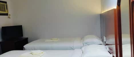 A hotel room with two beds, a wooden dresser, a mirror, a 'No Smoking' sign, and a water bottle.