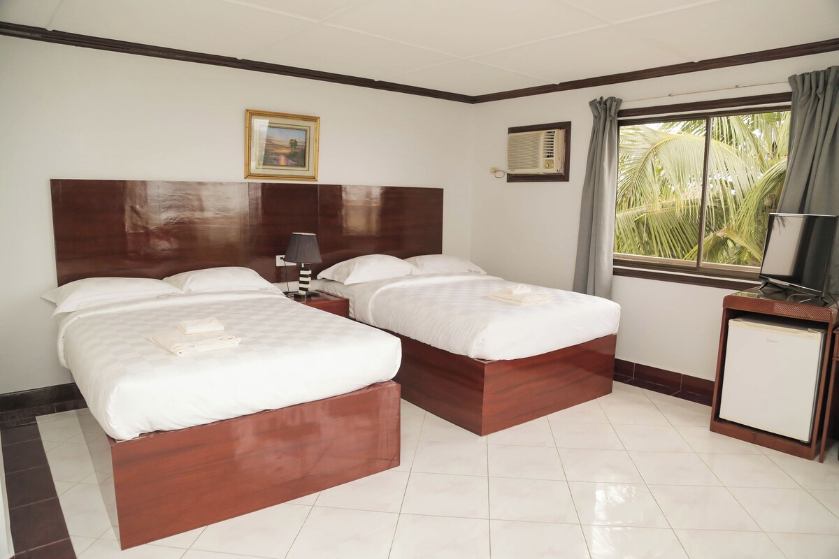 A hotel room with two beds, a nightstand, a TV, and a window with curtains.
