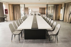A conference room with a long table and chairs, large windows with curtains, and a visible fire extinguisher.