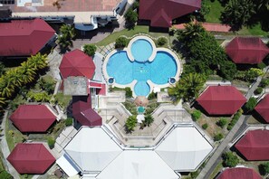 An aerial view of a hotel with a central swimming pool, multiple red-roofed buildings, and surrounding greenery. - Bohol Plaza Resort and Restaurant (Dauis)