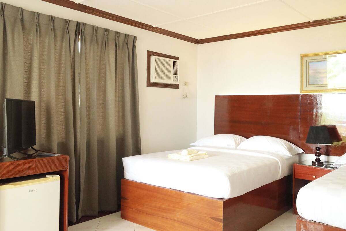 A hotel room with a wooden bed, a television on a desk, a desk lamp, and a window with curtains.