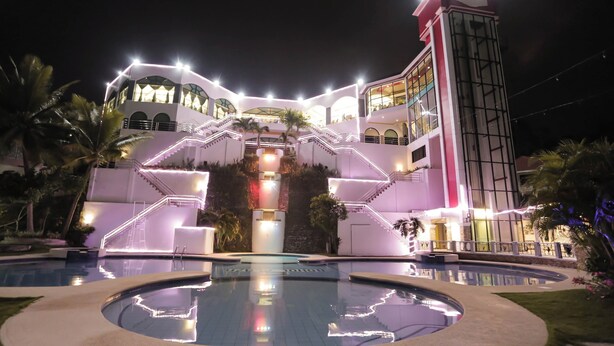 Un hotel de varios pisos con una escalera central, piscina y una torre alta.