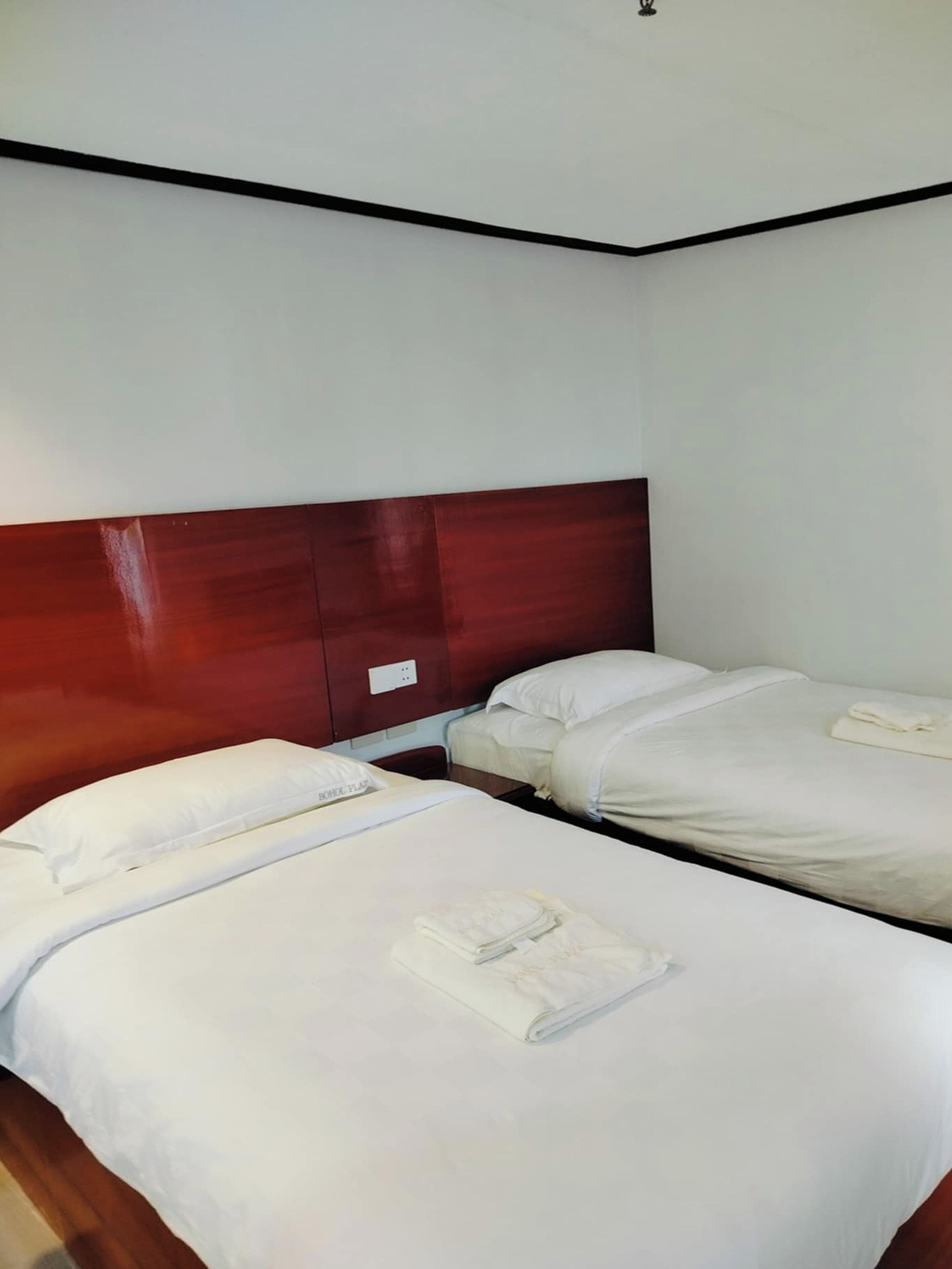 Habitación de hotel con dos camas, cabecero de madera, ropa de cama blanca y un enchufe a la vista.